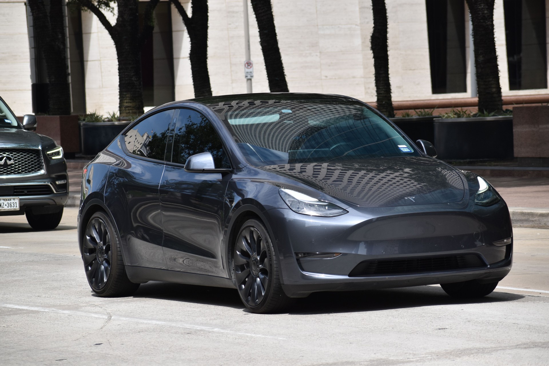 A portrait of a gray colored Tesla Model 3 cruising in a downtown district